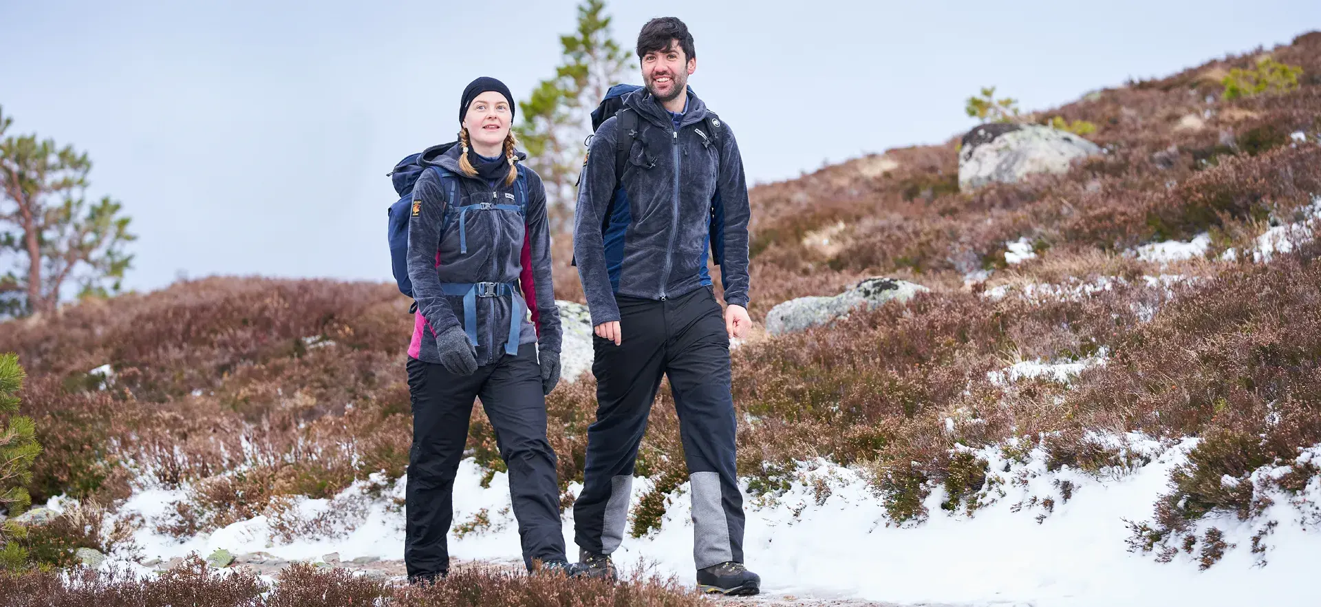 Couple hiking through a snowy moor wearing warm fleeces with backpacks