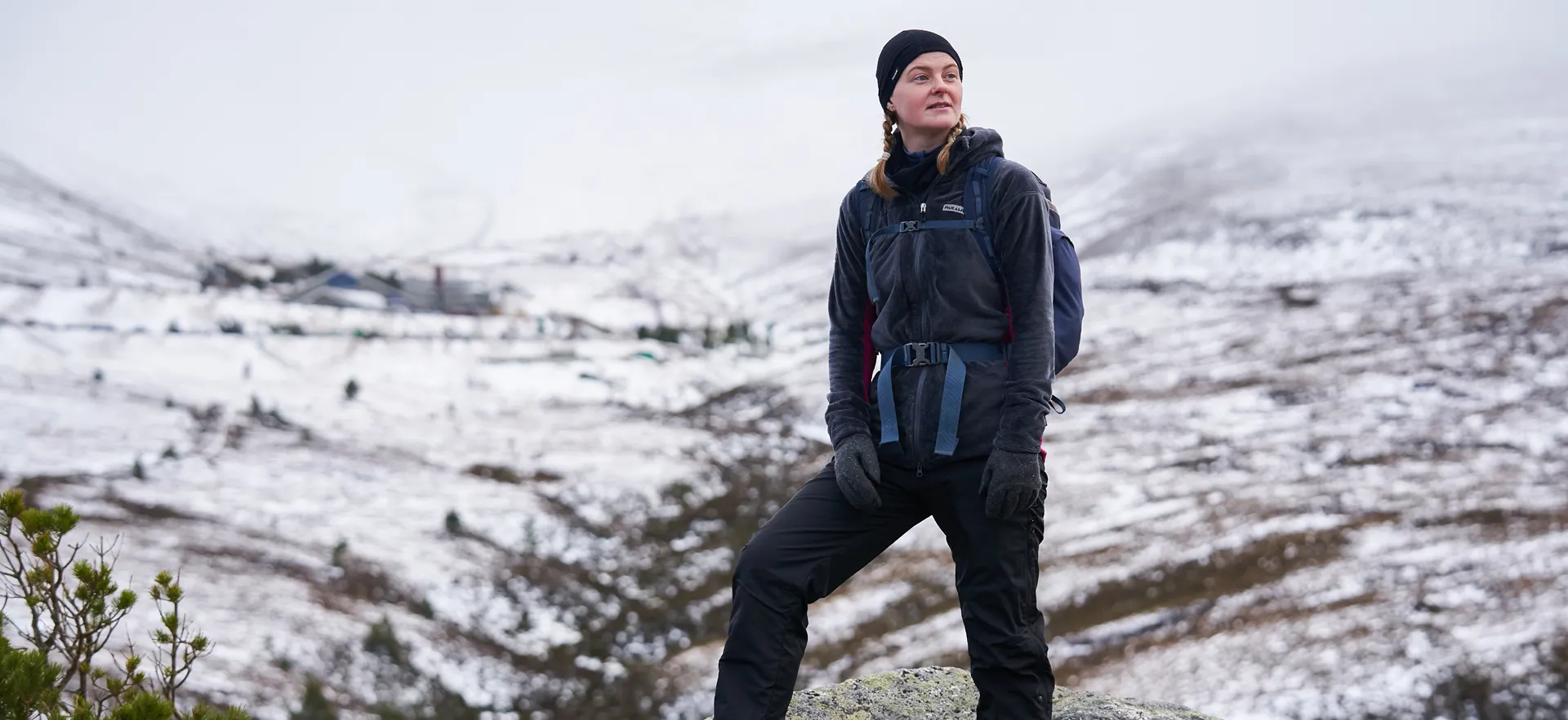 woman standing on a snowy moor wearing warm fleeces with backpacks looking around at the view