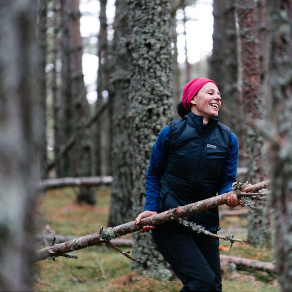 lady in the woods wearing a lightweight gilet and a baselayer, carrying wood