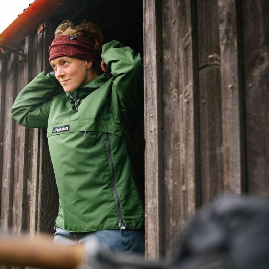 Woman in green, lightweight pullover jacket looking out of the doors of a cabin