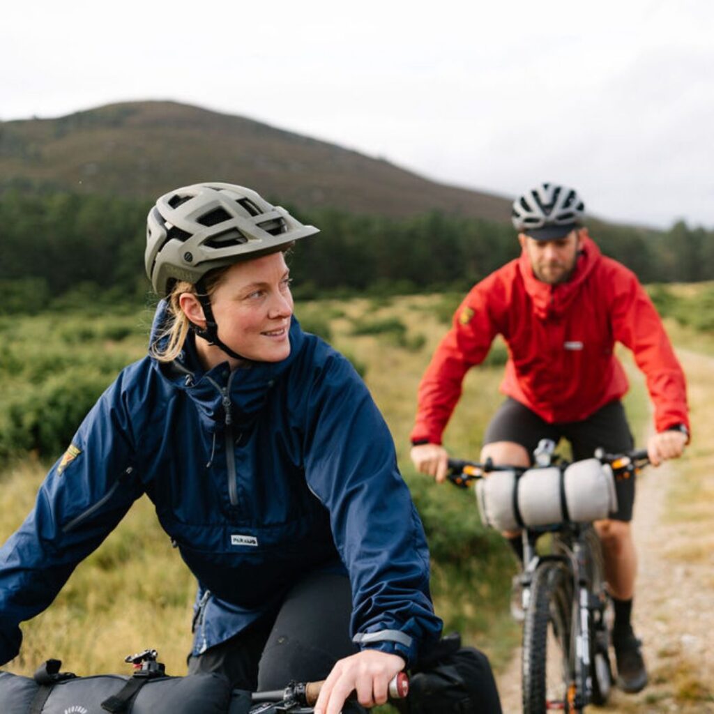 Man and woman cycling in the grassland, wearing lightweight jackets 