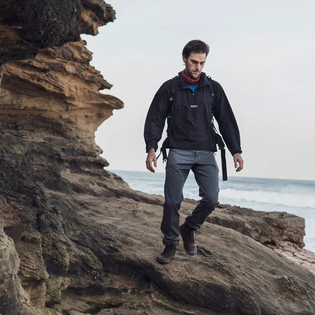 Man in Páramo Fuera Windproof Smock walking on the shoreline clifftop 
