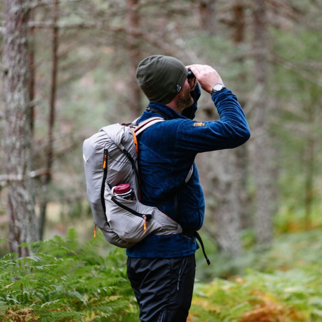 Man in the woods using binoculars to view the trees