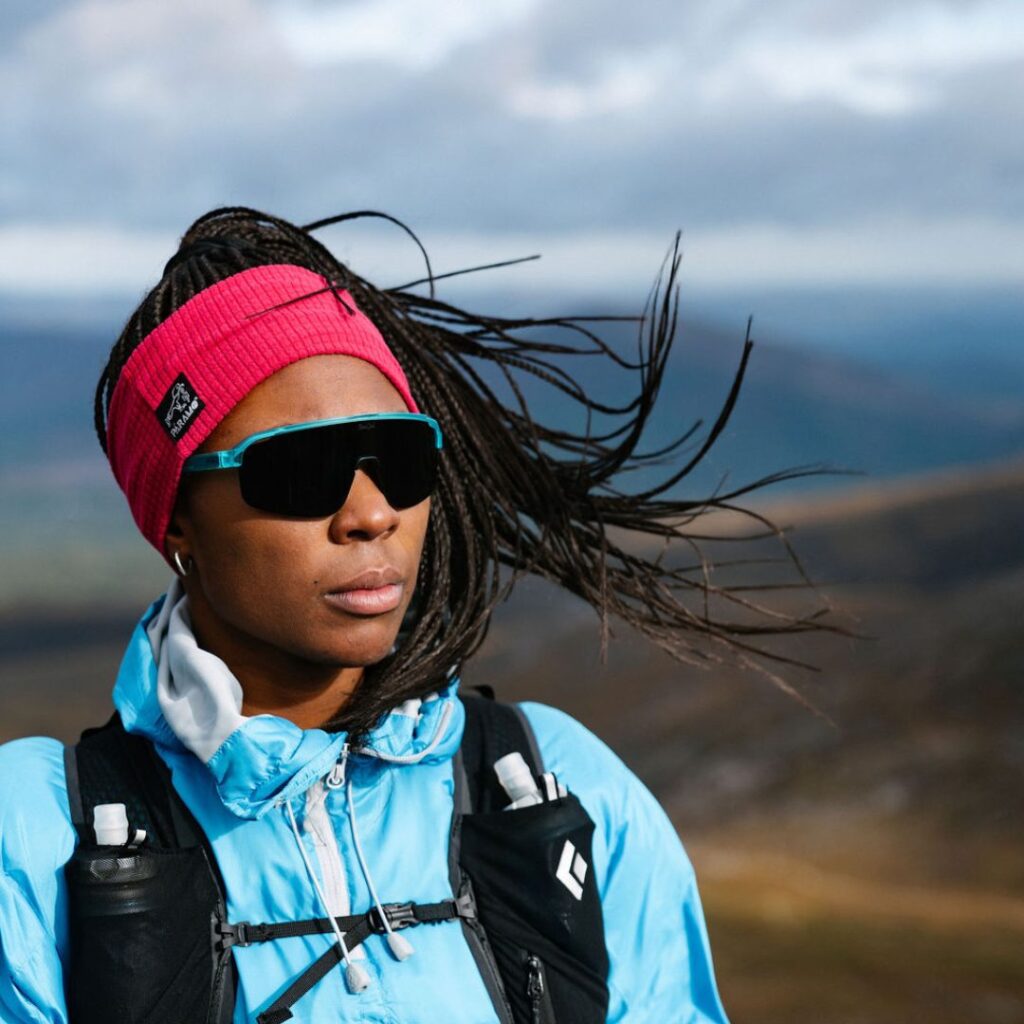 Woman atop a sunny mountainside, sunglasses on, taking in the view 